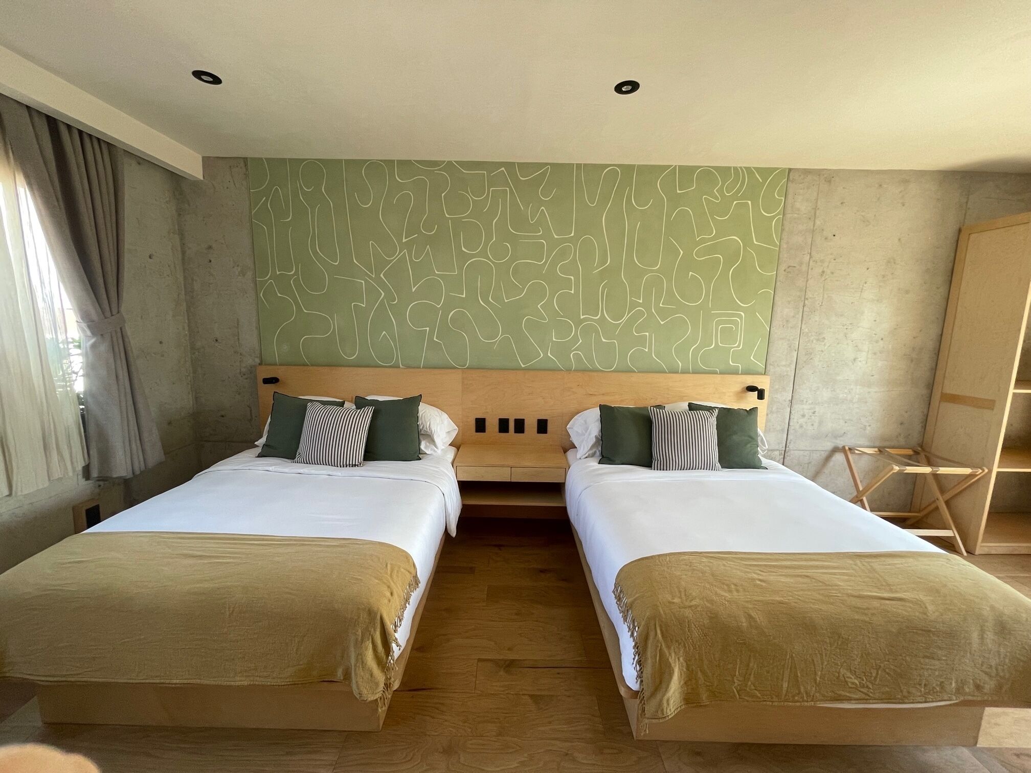 Habitació d'hotel amb dos llits, ambres de fusta i un disseny abstracte verd a la paret.