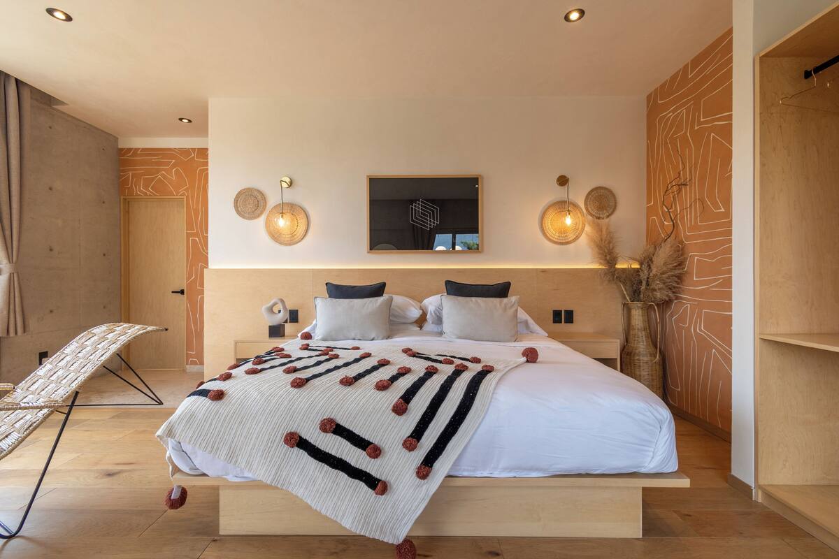 A modern bedroom with a large bed, a wall-mounted TV, and a decorative wall panel.