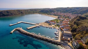 An aerial view of a coastal town with a marina, houses, and a hilly landscape.