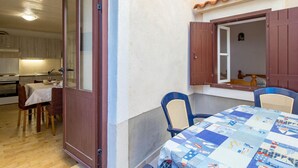 A compact kitchen with a dining area, a wooden table with a quilt, and a window with shutters.
