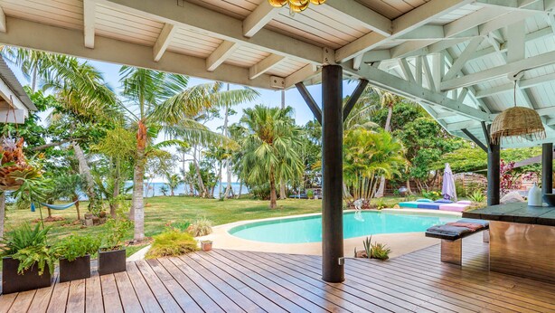 Una terraza de madera con piscina, rodeada de plantas tropicales y palmeras.