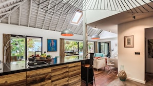 Una cocina moderna con una isla de madera, iluminación colgante y ventanas amplias que dan a un jardín.