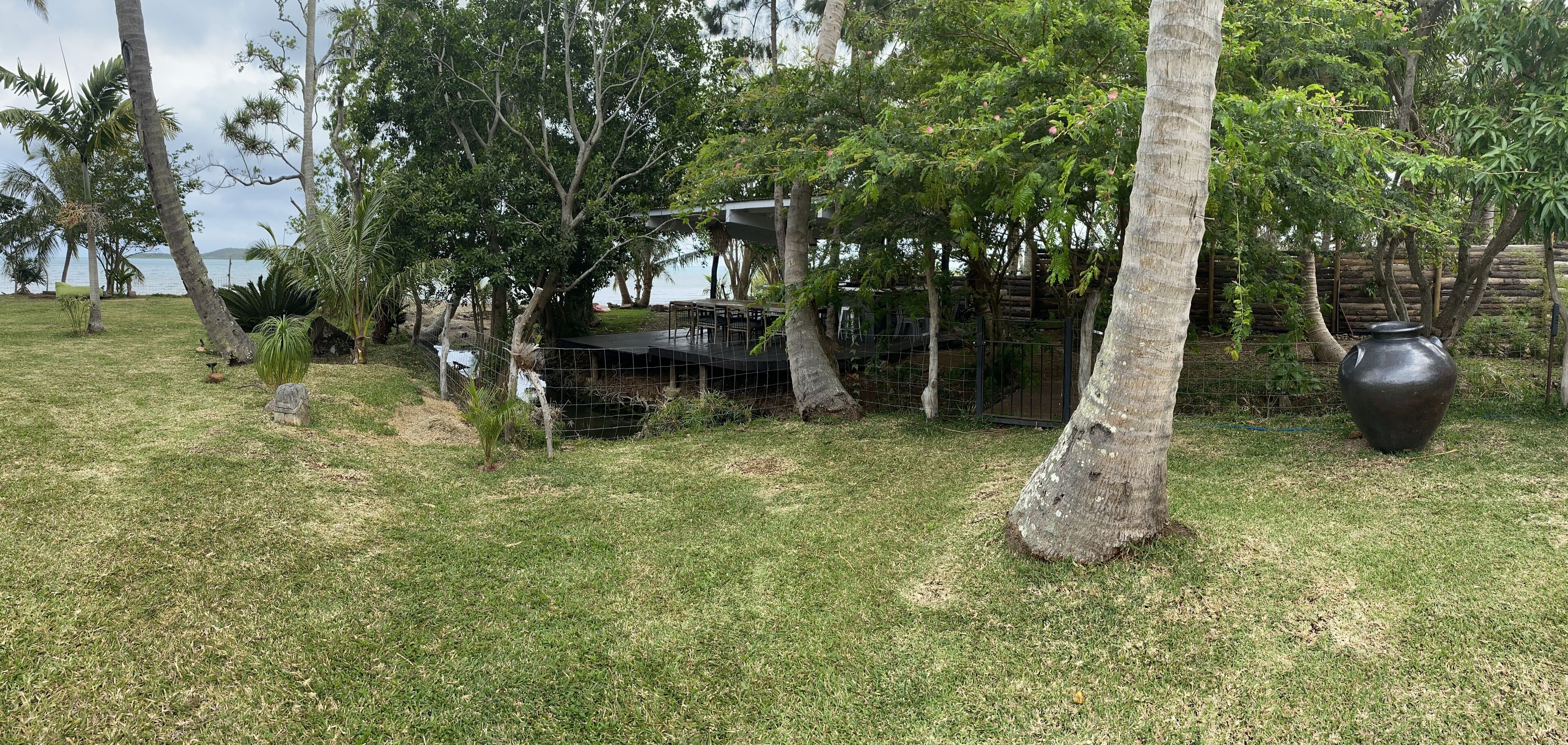 A grassy outdoor area with trees, a wooden structure, and a large pot.