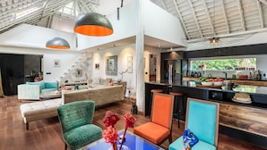 Amplia sala de estar con techo alto, muebles modernos y una cocina visible al fondo.