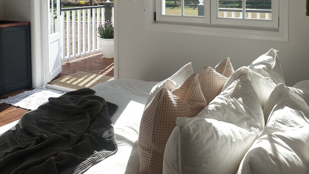Un dormitorio con cama, almohadas, una ventana y una puerta que da a un balcón.