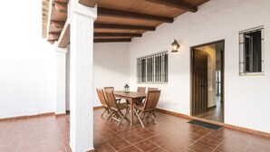 Un comedor con mesa y sillas de madera, suelo de baldosas y una ventana con barrotes.