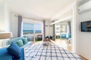 Un dormitorio con una cama grande, vistas a la ciudad, un balcón con mobiliario y un televisor montado en la pared.