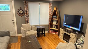 A living room with a wooden floor, a sofa, a chair, a small table, a bookshelf, a television, and a fireplace. - Lexington Stays. Close to town and beach!  (Lexington)