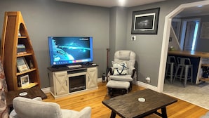 A living room with a flat-screen TV, a fireplace, a cushioned armchair, and a wooden coffee table. - Lexington Stays. Close to town and beach!  (Lexington)