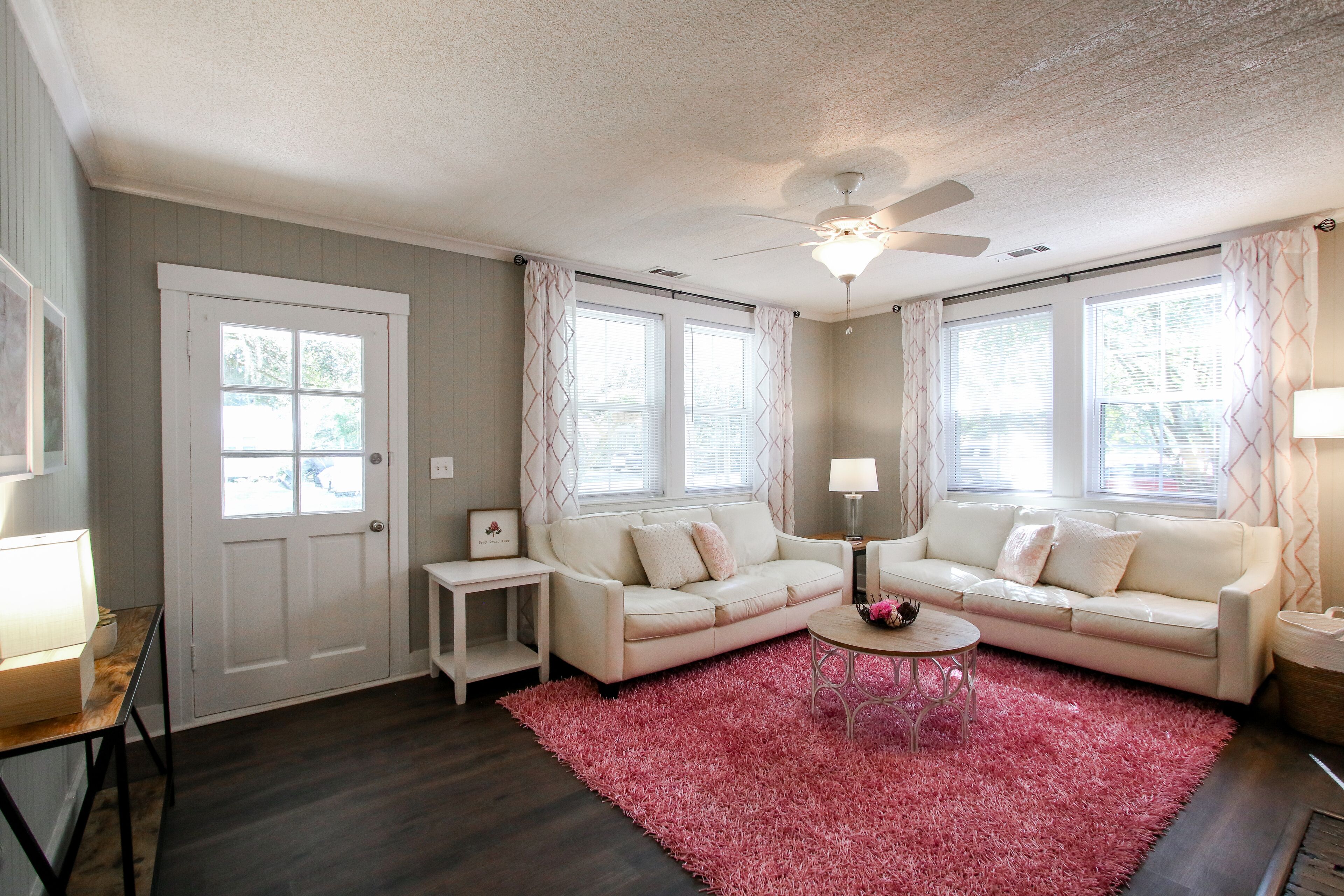 A living room with a white sofa, a small side table, a pink rug, and a ceiling fan.