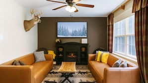 A cozy living room with two brown leather sofas, a wooden coffee table, a fireplace, and a deer head mounted on the wall. - The Ravine • Hot Tub Forest Escape, Epic Gameroom, Fast WIFI & Pet Friendly (Basye)