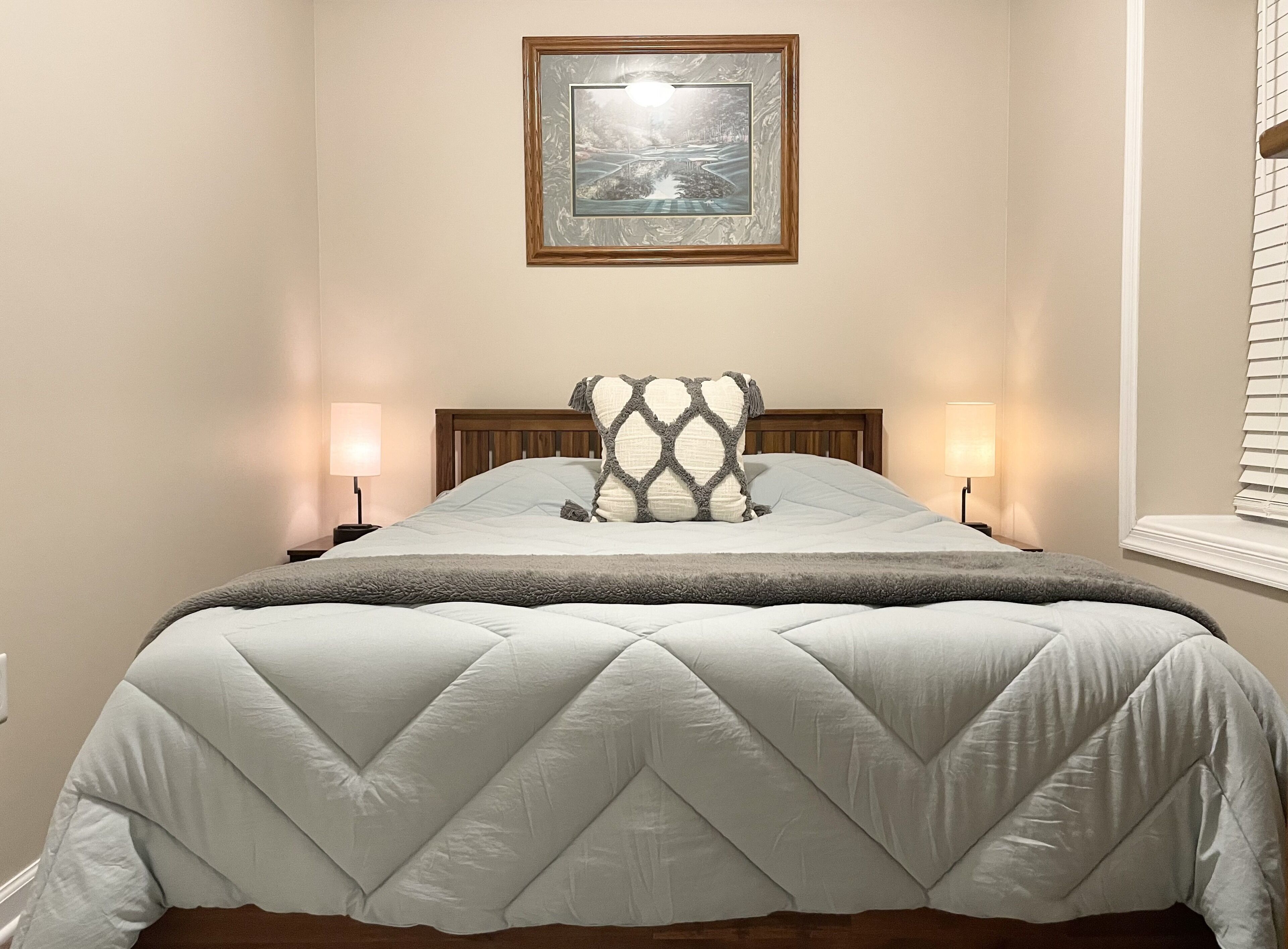 A neatly made bed with a quilted bedspread, two bedside lamps, and a framed picture on the wall.