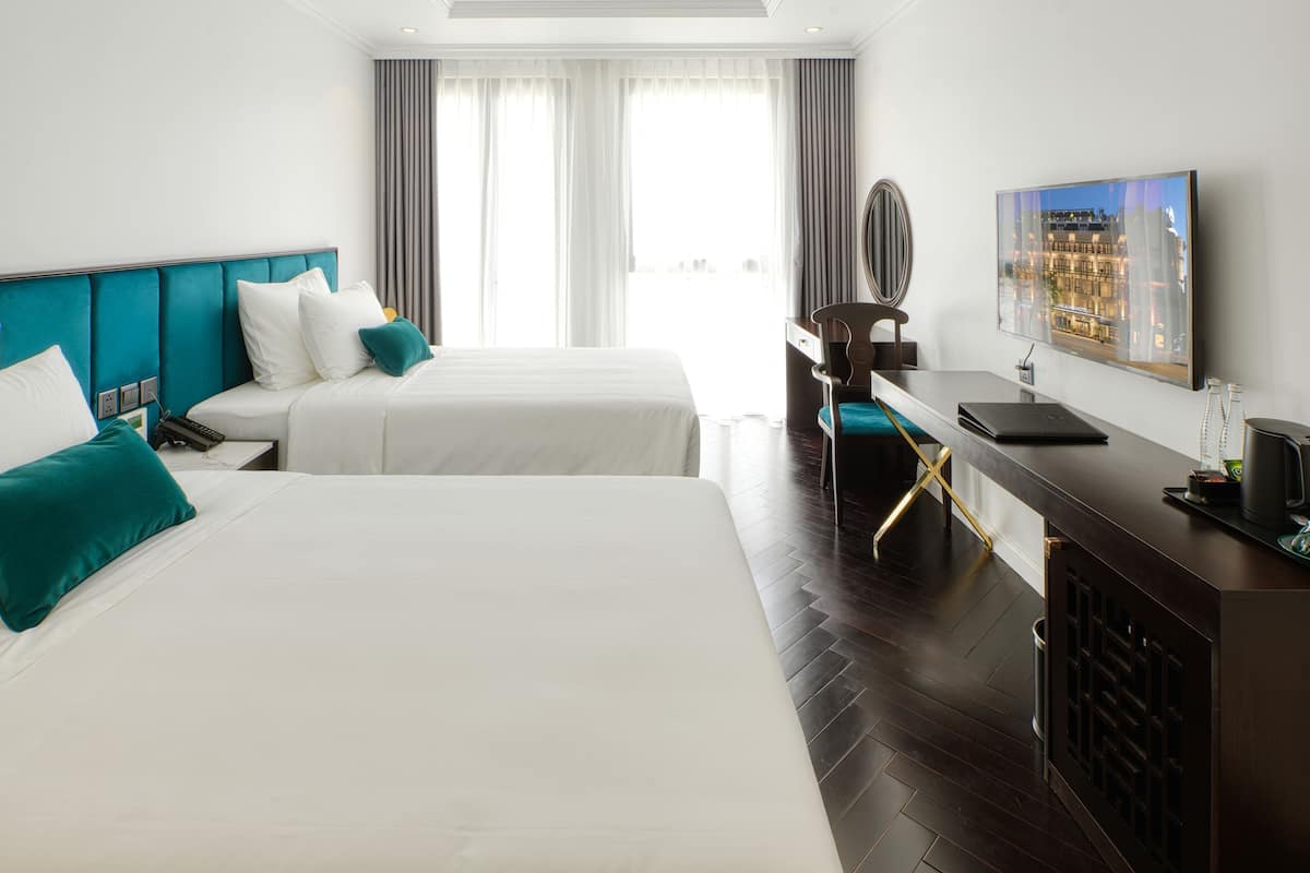 A hotel room with two beds, a desk, a chair, a television, and a window with curtains.