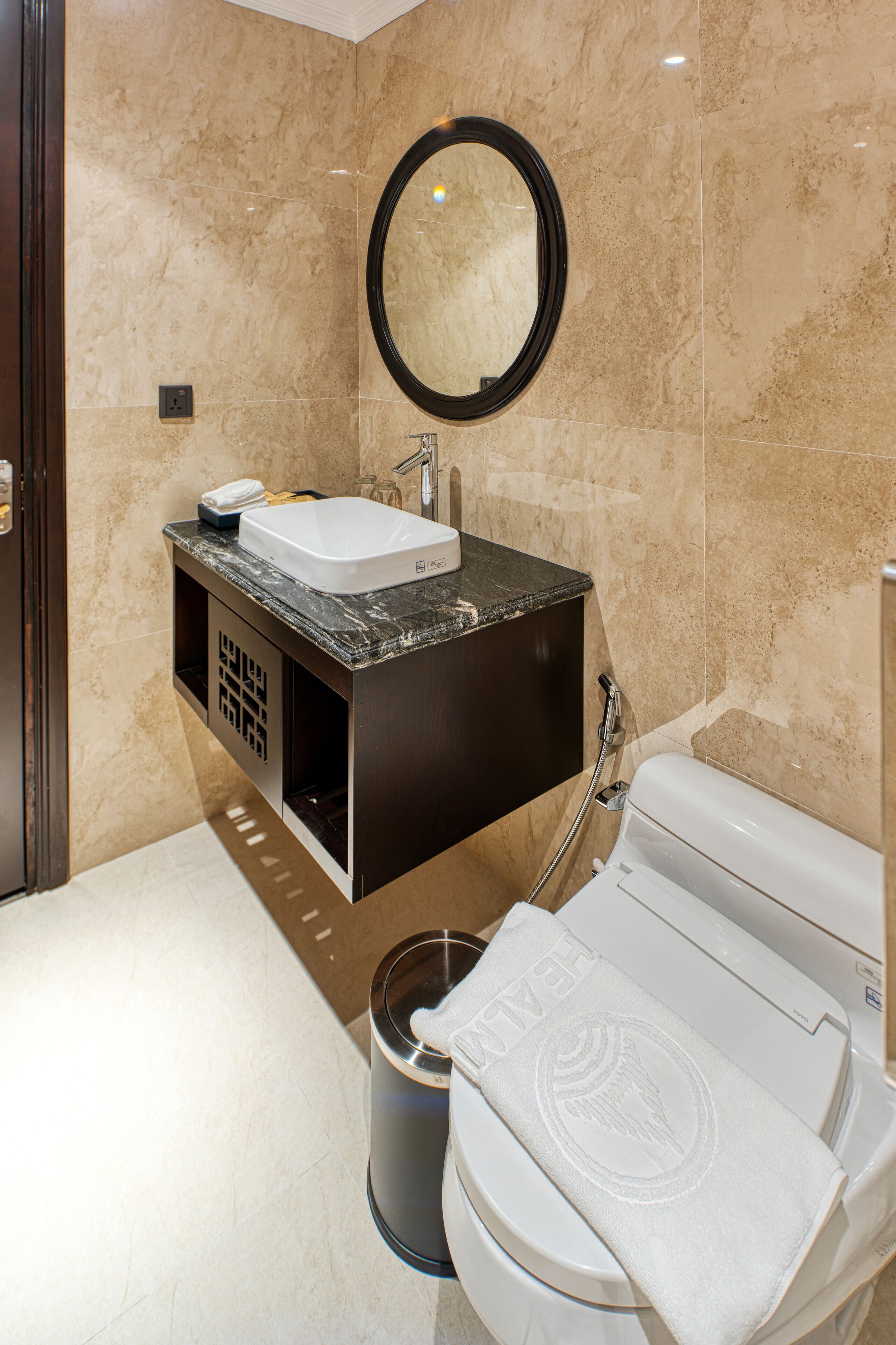 Ein modernes Badezimmer mit Marmorwand, Waschbecken mit schwarzer Arbeitsplatte, Spiegel und Toilette mit Handtuch.