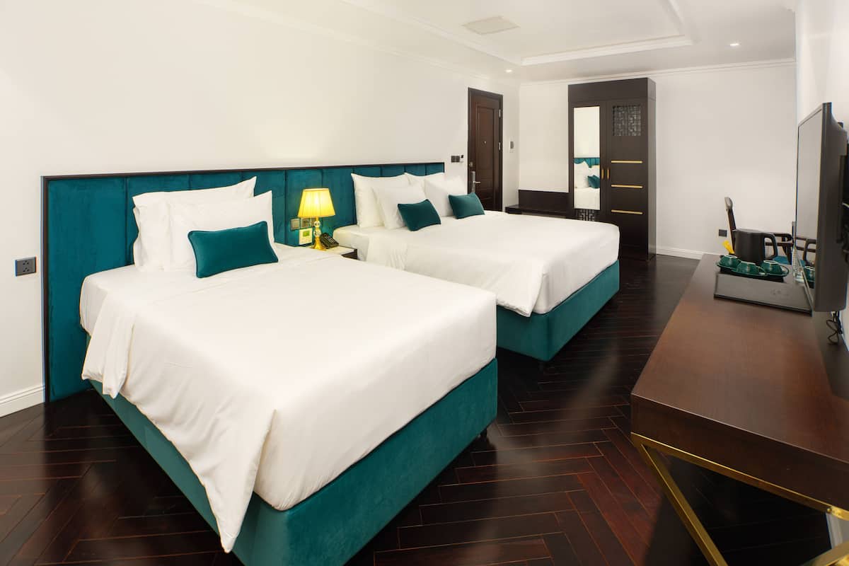 A hotel room with two beds, a desk, a TV, and a door leading to another room.
