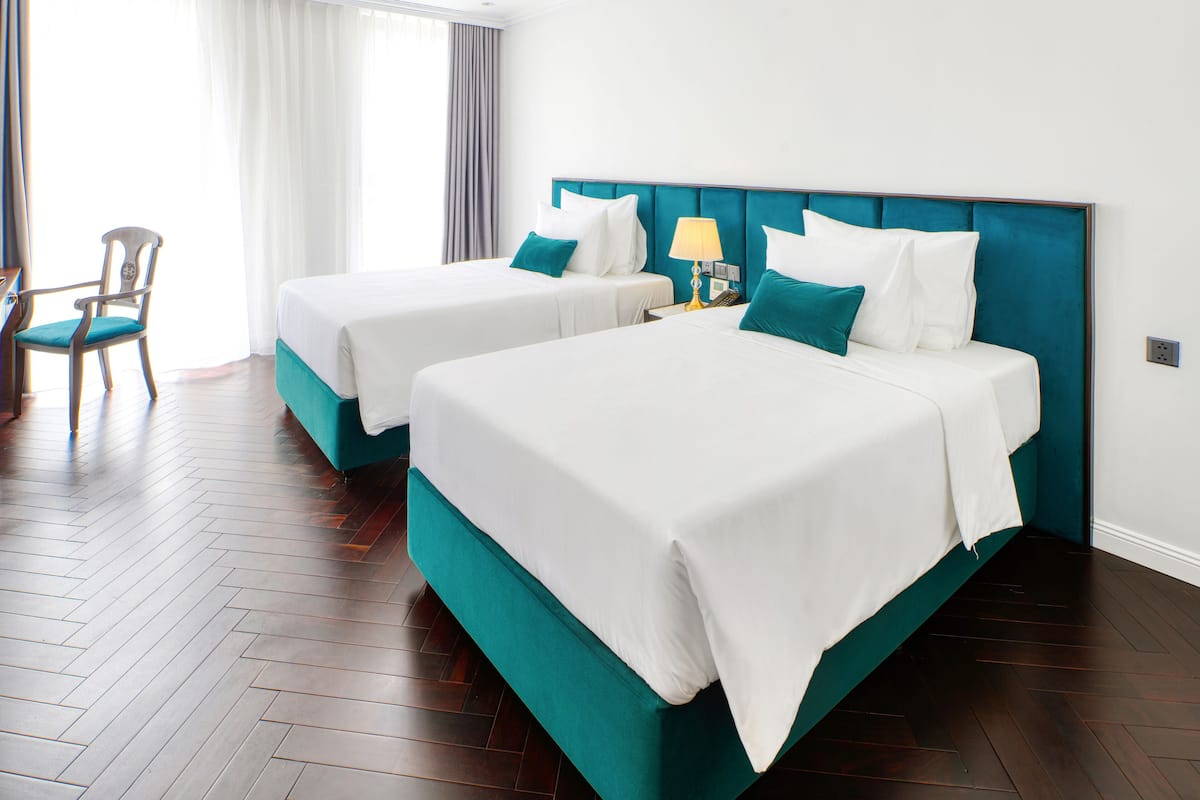 A hotel room with two beds, a chair, and a nightstand with a lamp.
