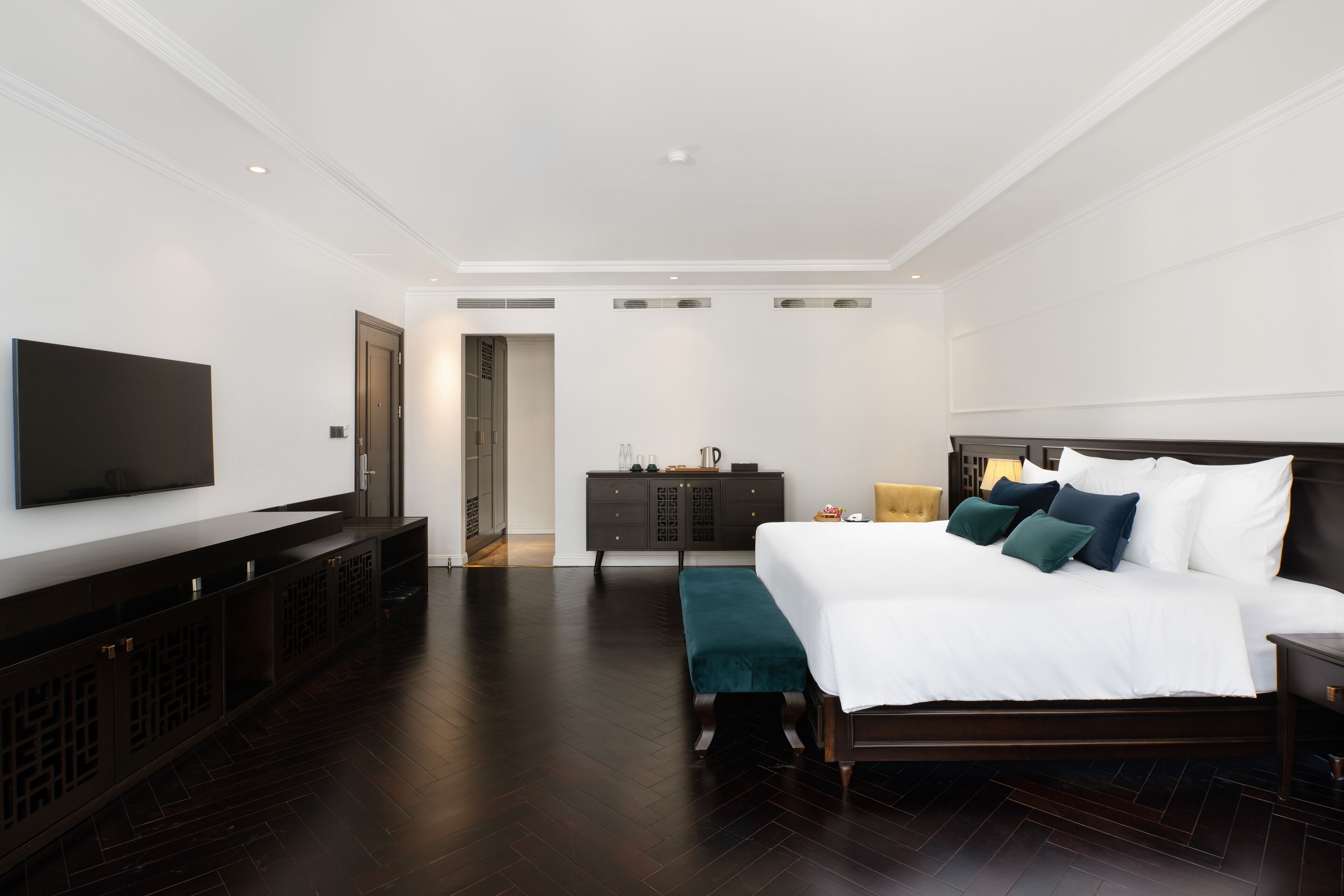 Una habitación de hotel moderna con una cama grande, un televisor, un aparador de madera oscura y un banco.