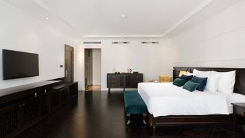 Una habitación de hotel moderna con una cama grande, un televisor, un aparador de madera oscura y un banco.
