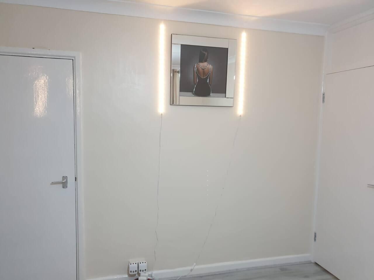 A room with a white door, a framed picture on the wall, and a light switch on the wall.