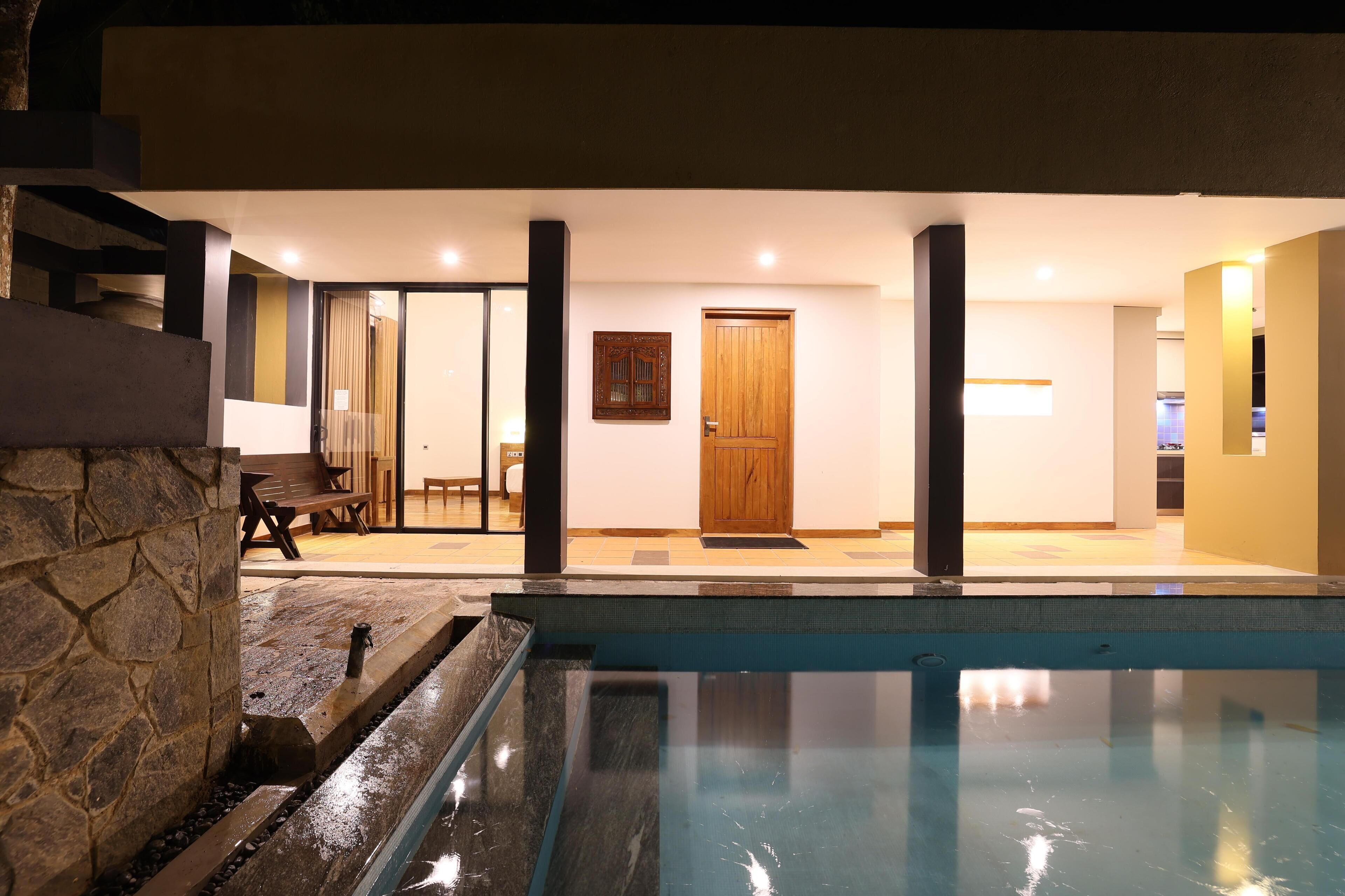 A swimming pool with a stone wall on one side, a wooden door, and a bench in the background.