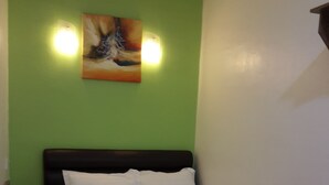 Una cama bien hecha con sábanas blancas y una manta marrón, un cuadro en la pared y una pared verde.