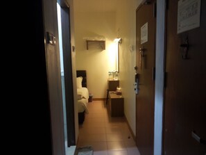 A narrow hallway with a bed, a nightstand, and a small table with a lamp. - GOLDEN GATE HOTEL (Chukai)