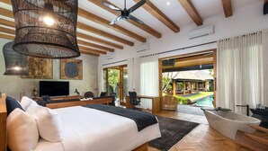 A spacious bedroom with a large bed, a desk, and a view of an outdoor pool area. - Villa Wolfe by Villa Finder (Seminyak)