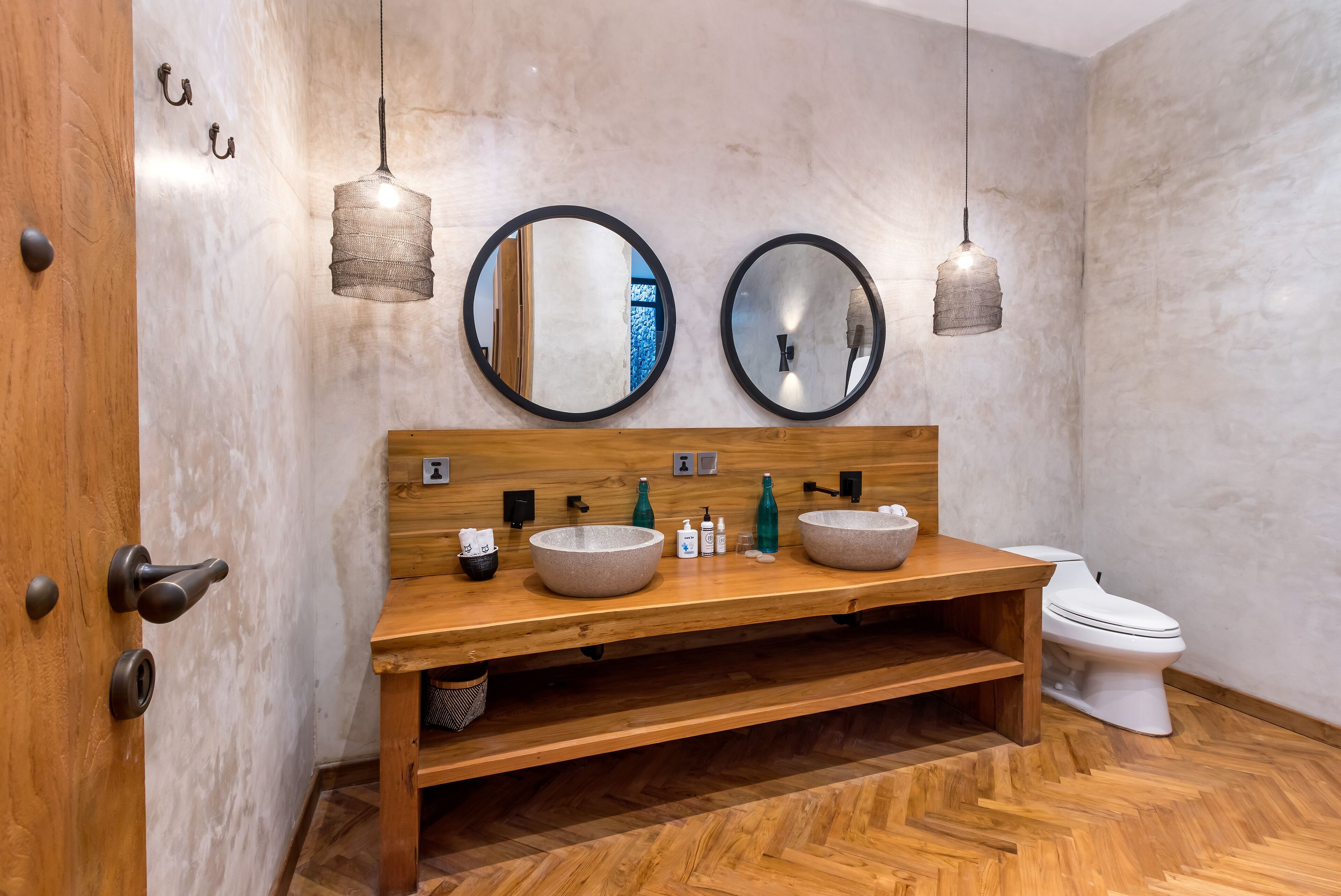 Une salle de bain avec un meuble-lavabo en bois, deux miroirs ronds et des toilettes blanches.