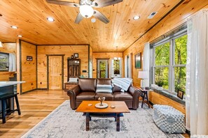 Relax in this cabin-style room with a high ceiling, leather sofa, and large window offering a view of the surrounding forest.