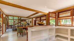 Una habitación amplia con techo de madera, un comedor con mesa y sillas, y ventanas grandes con contraventanas de madera.
