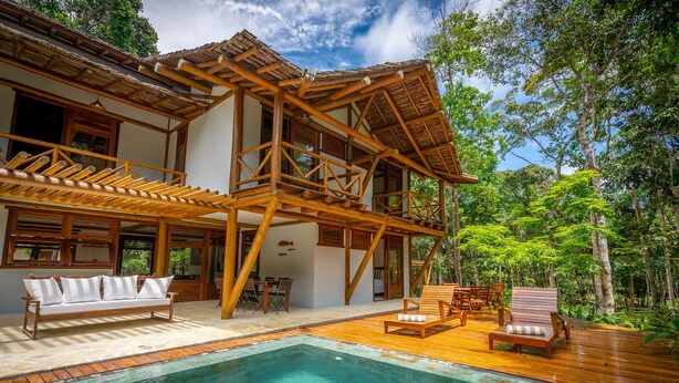 Una casa de madera con piscina, mobiliario exterior y un exuberante jardín.