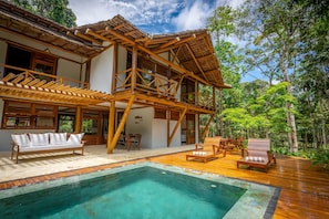 Una casa de madera con piscina, mobiliario exterior y un exuberante jardín.