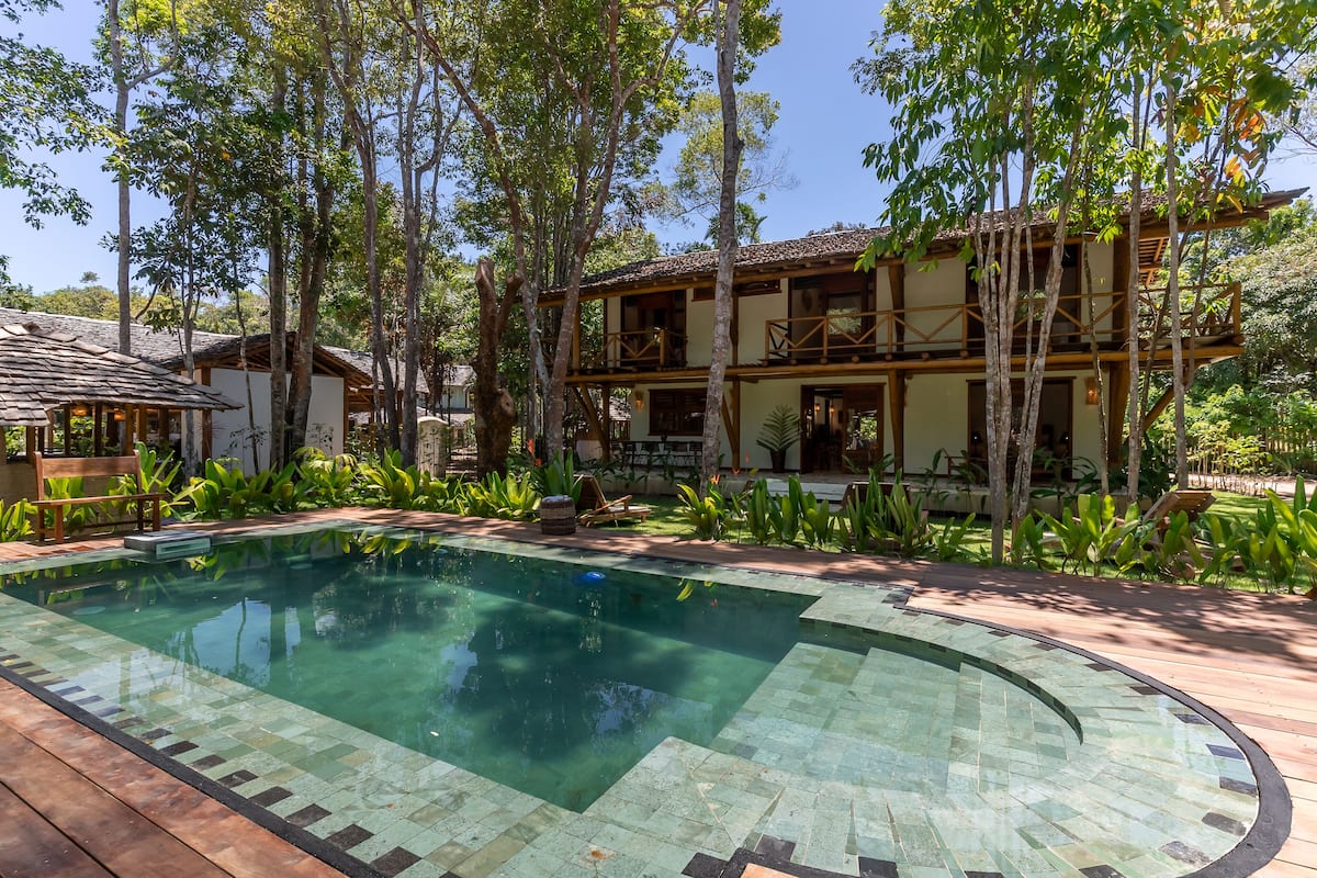 Una piscina rodeada por una terraza de madera, con un edificio de dos pisos al fondo.