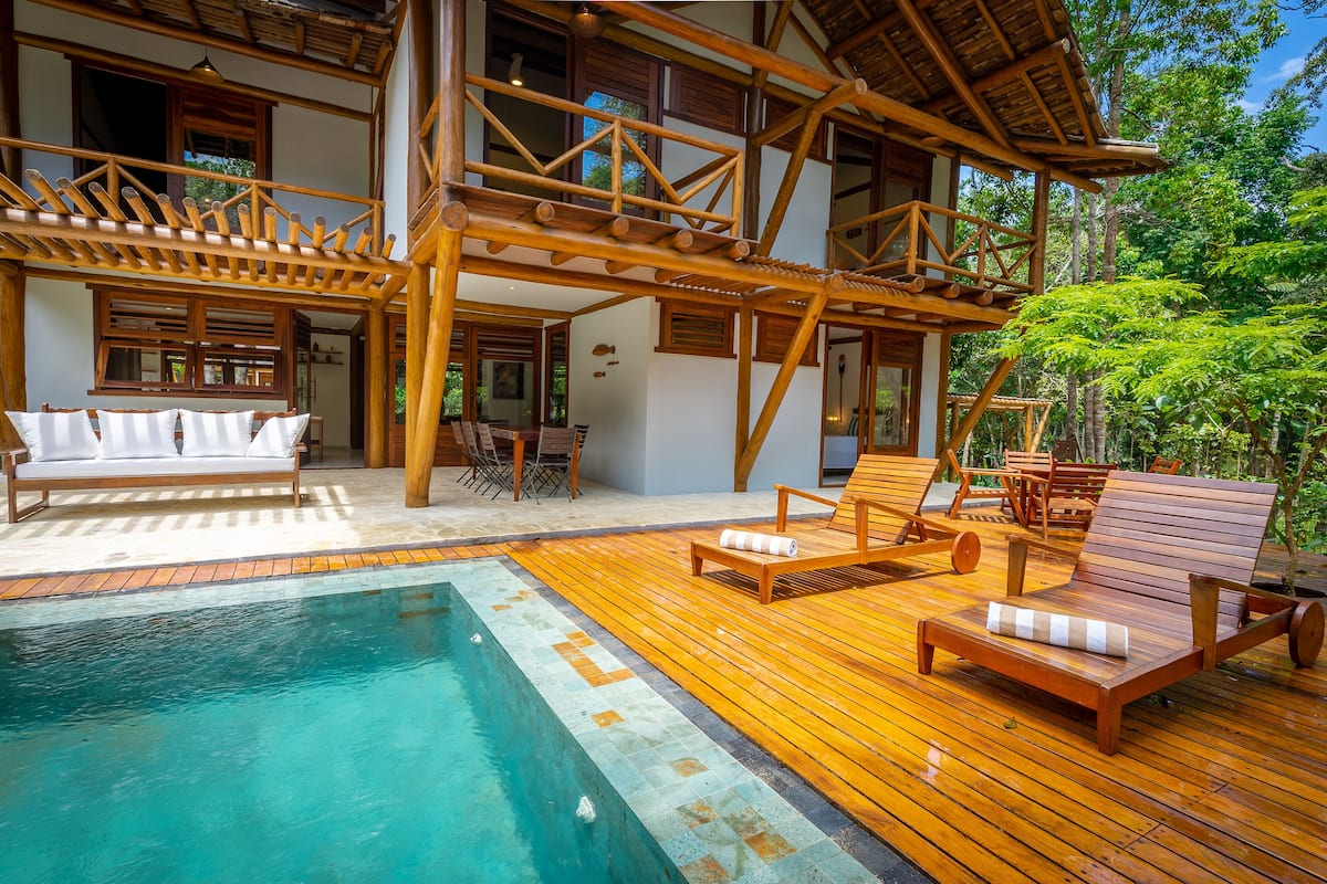 Una terraza de madera con piscina, sillas de descanso y una pérgola de madera.