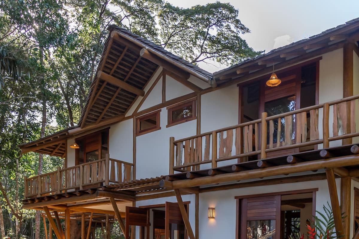 Una casa de madera de dos pisos con balcón, piscina y una cesta de mimbre con toallas.