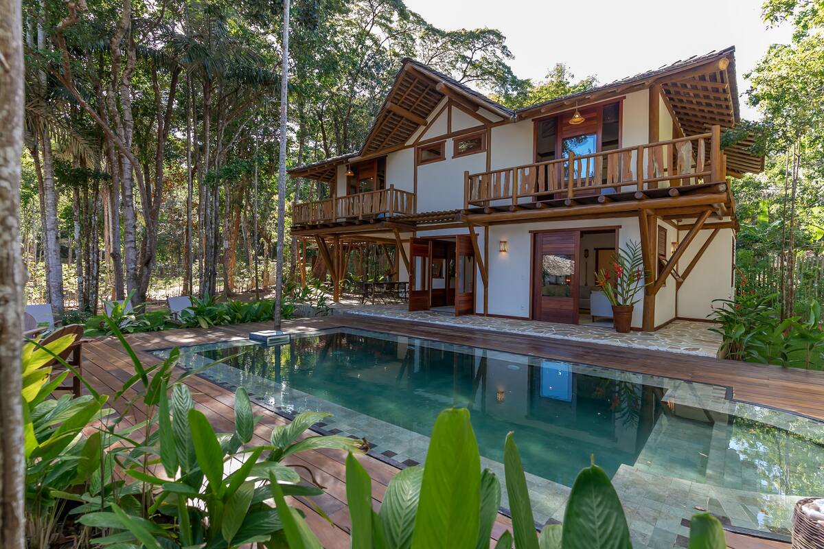 Una casa de dos pisos con piscina, rodeada de abundante vegetación.