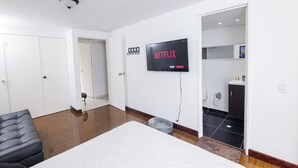 Ein modernes Hotelzimmer mit Bett, einer Sitzecke, einem an der Wand befestigten Fernseher und einem durchgegangenen Badezimmer.