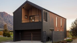 A modern two-story house with a large garage, wooden interior, and a view of mountains. - Beautiful 3 bedroom home | Hot Tub | Stunning View (Jacks Point)