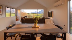 A modern dining area with a large table and chairs, a sofa with cushions, and a potted plant. - Beautiful 3 bedroom home | Hot Tub | Stunning View (Jacks Point)