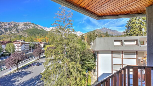 Un balcone con vista su una montagna, un'area parcheggio e degli edifici.