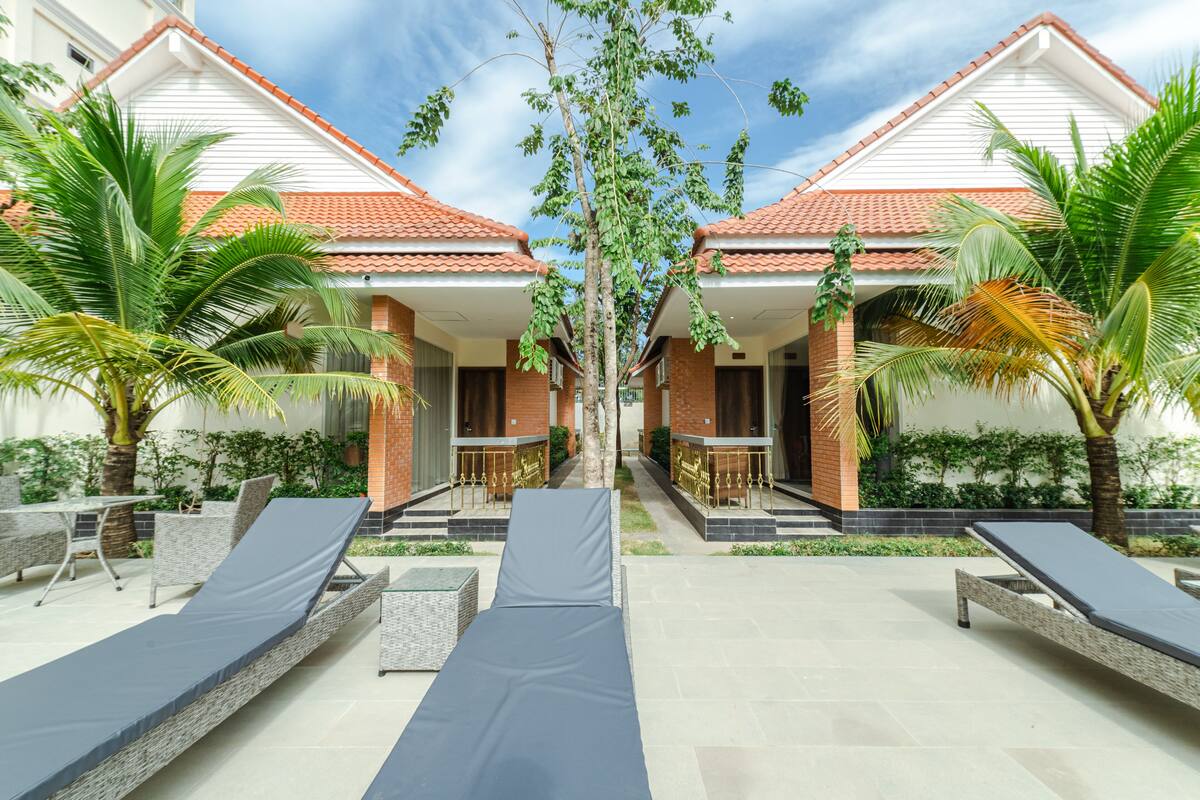 Een resort met twee verdiepingen tellende gebouwen, buitenzitplaatsen met ligbedden en palmbomen.