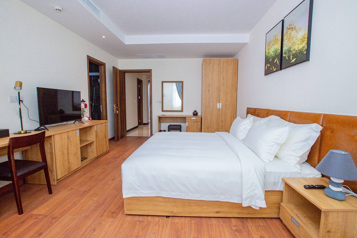 Een slaapkamer met een bed, nachtkastje, lamp, televisie, houten bureau, stoel en kledingkast.