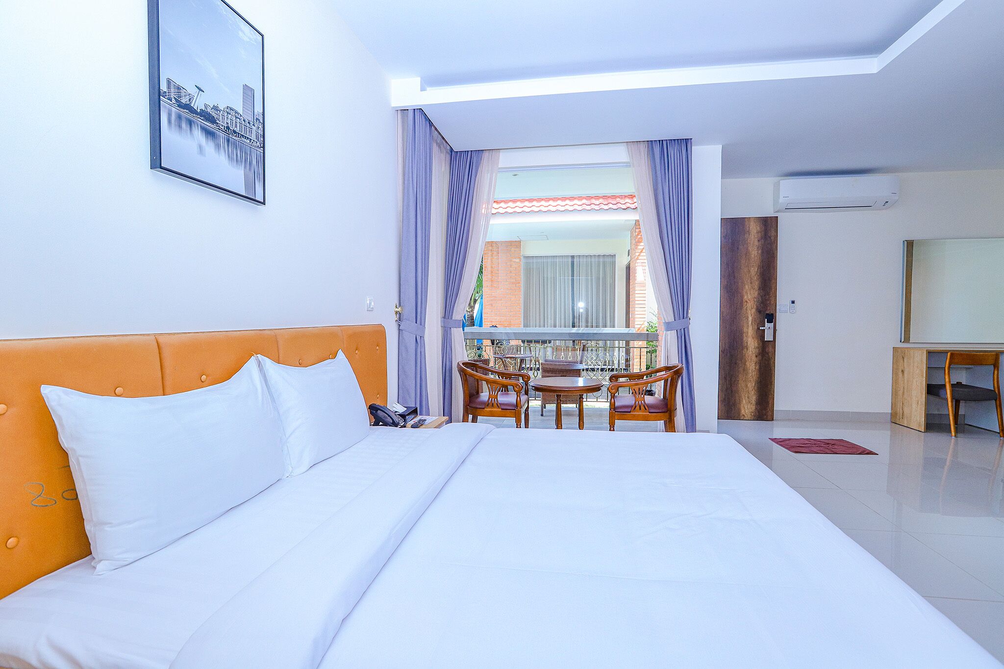 Hotelkamer met een groot bed, een houten hoofdbord, een balkon met een tafel en stoelen, en uitzicht op de stad.