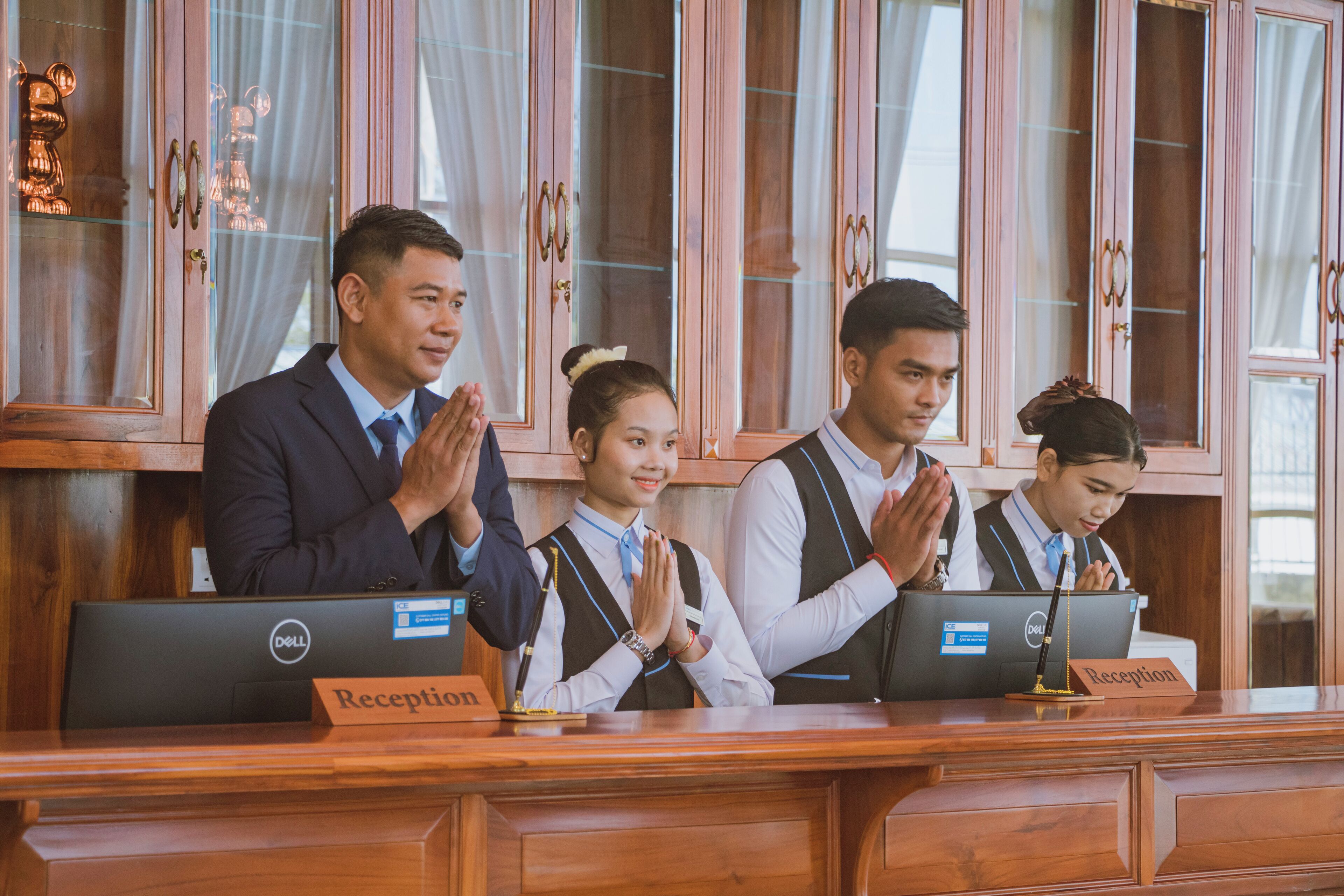 A reception desk with a nameplate labeled "Reception" and three individuals seated behind it, one of whom is using a laptop.
