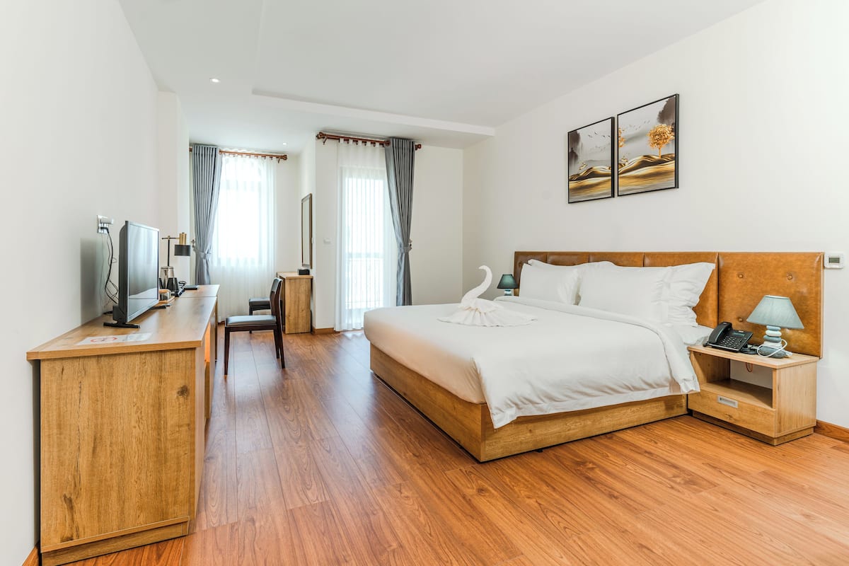 Een hotelkamer met een houten bed, een bureau met een computer, een televisie en een nachtkastje met een lamp.
