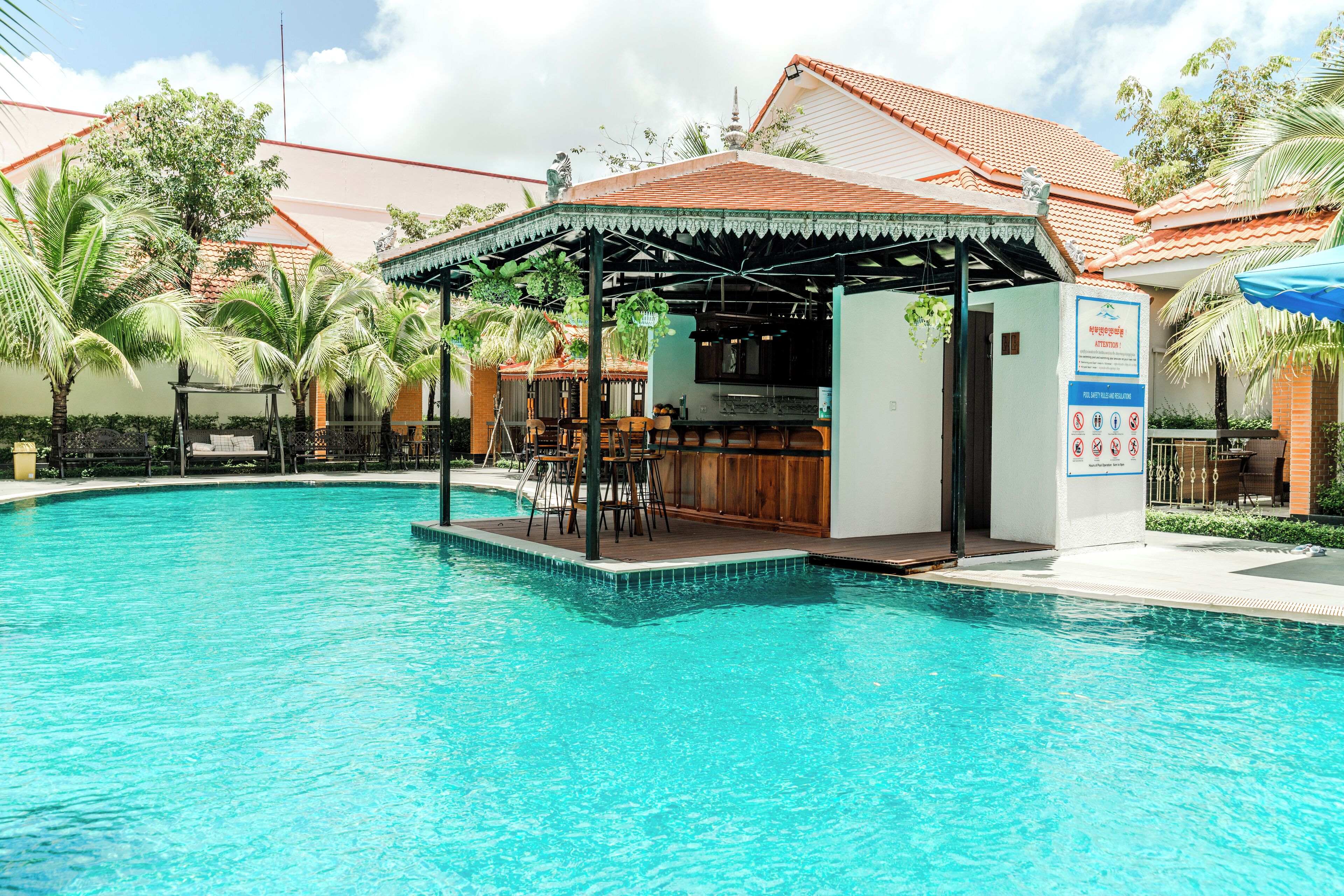 A swimming pool with a bar area, surrounded by palm trees and a covered seating area.
