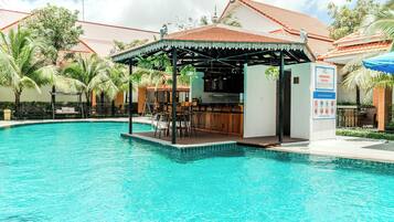 A swimming pool with a bar area, surrounded by palm trees and a covered seating area.