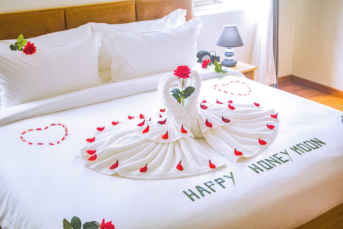 Een net opgemaakt bed met een handdoek in de vorm van een zwaan, een roos en de tekst 'HAPPY HONEY MOON' op het beddegoed.