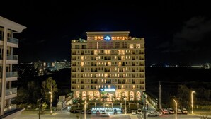 Een hotel met meerdere verdiepingen, een opvallend bord, een parkeerplaats en een uitzicht op de skyline op de achtergrond.