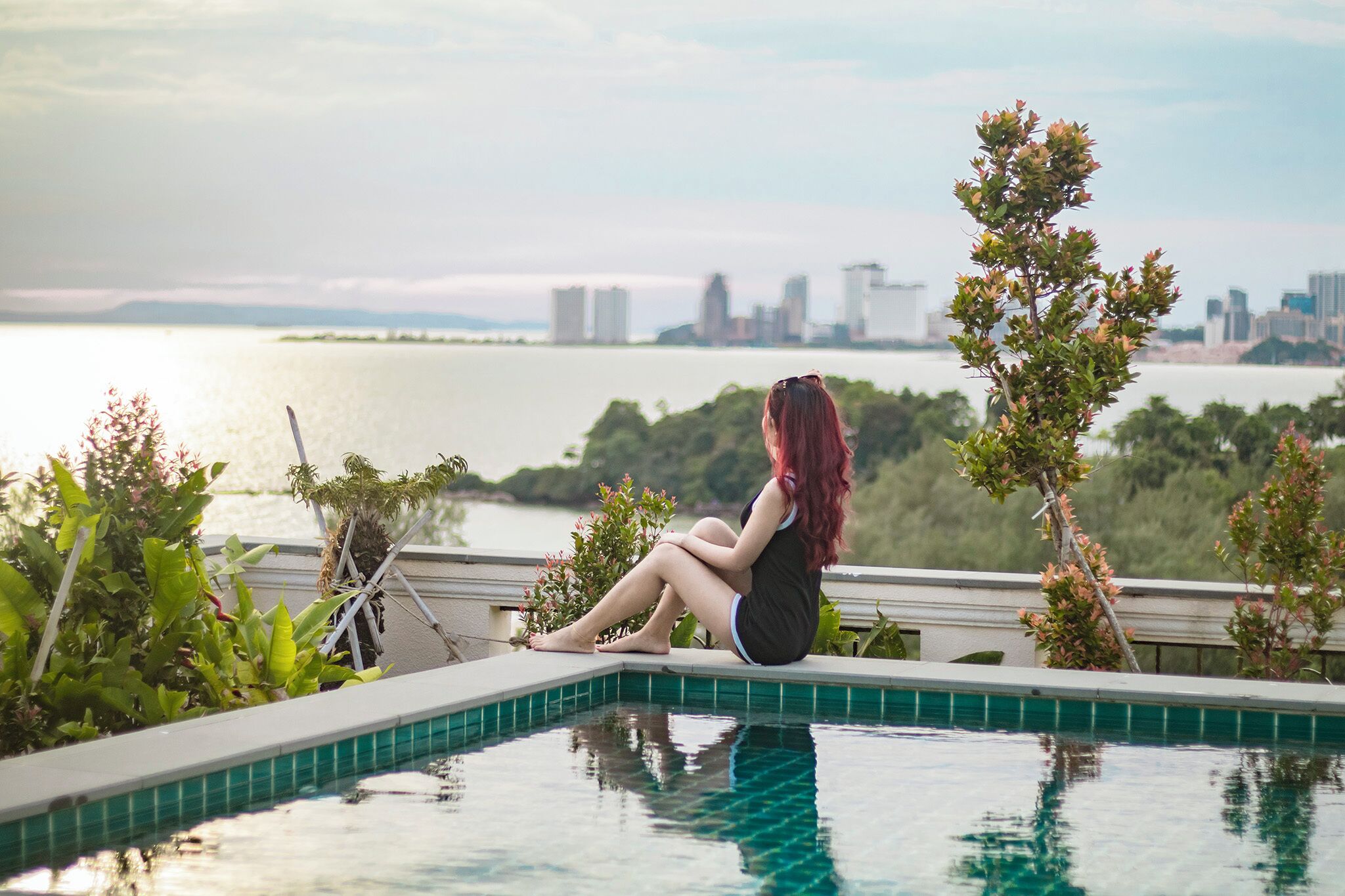 Una persona sentada junto a una piscina, con un horizonte urbano al fondo.